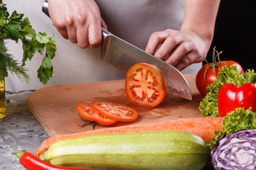 young woman slicing a tomato in a gray apron