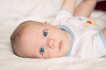 Baby boy with blue eyes looking up laying on bed