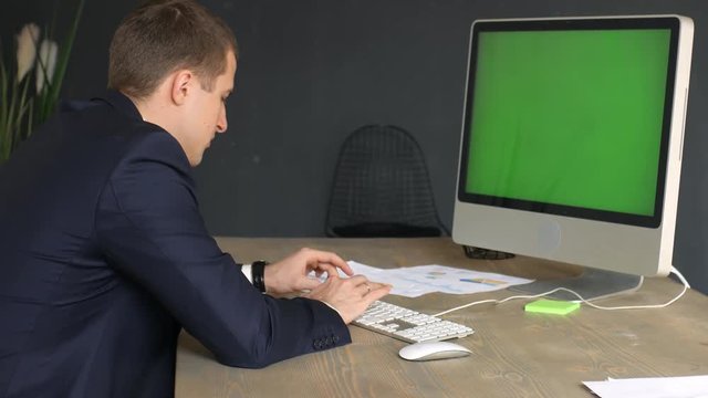 man in a suit working behind a monoblock with a green screen in the office, typing on the keyboard