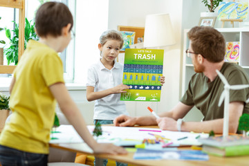 Resolute blonde little boy carrying educative poster about trash recycling