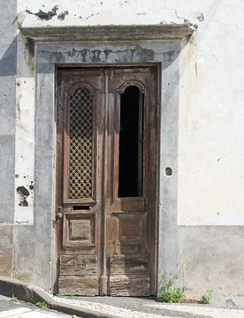 and old elegant weathered ornate wooden brown door with carved panels and missing grille in a white abandoned house