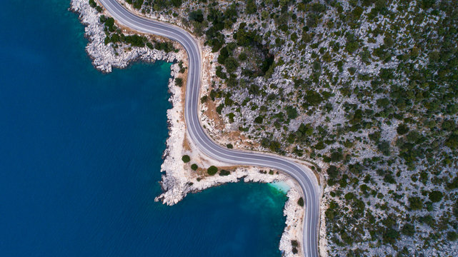 Aerial landscape of coastline and a road seascape. Car drives down the empty asphalt road running along the sunny Mediterranean shoreline of Turkey. Tourist car cruises down the scenic coastal road . © yusufozluk