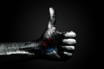A hand with a drawn South Korea flag shows a finger up sign, a symbol of success, readiness, a task done on a dark background.