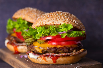 Two delicious homemade beef burgers with bacon on wooden chopping board