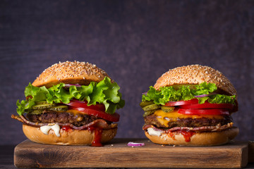 Two delicious homemade beef burgers with bacon on wooden chopping board. Room for text. Food background