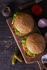 Two delicious homemade beef burgers with bacon on wooden chopping board. View from above, top studio shot