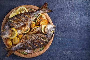 Roasted fish and potatoes, served on wooden tray. overhead, horizontal, copy space - image