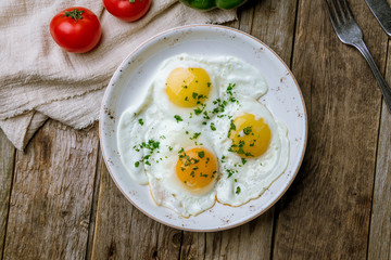 Fried eggs with tomatoes on wooden background