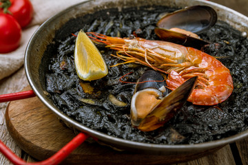 black paella with seafood on wooden background