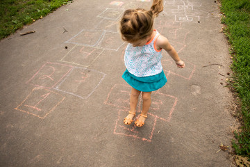A toddler aged girl playing hopscotch outside in a park.