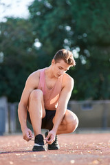 Young man runner tying shoelaces on stadium.