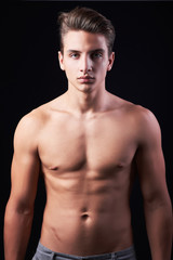 Fototapeta premium Studio portrait of handsome muscular shirtless young man isolated on black