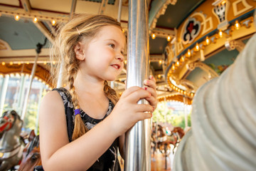 A toddler aged girl riding on a horse carousel in a them park.