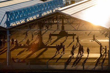 A group of people playing basketball at a outdoor gym during sunset.