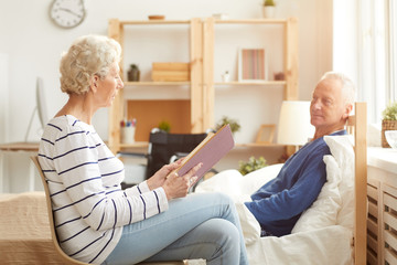 Side view portrait of elderly couple enjoying retirement, focus on wife reading book aloud to white...