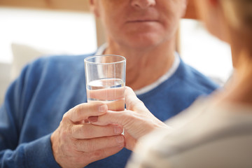 Closeup of senior man taking glass of water from wife supporting him, copy space