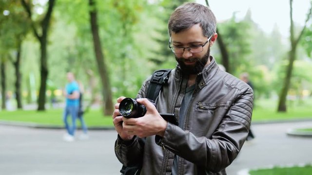 Happy bearded man with camera takes a photo in the park, blogger takes vlog