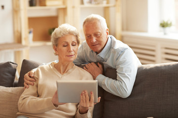 Portrait of modern senior couple using digital tablet  at home lit by sunlight, copy space