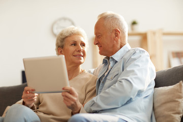 Low angle portrait of modern senior couple using digital tablet  at home lit by sunlight, copy space