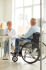Full length portrait of female doctor consulting senior man in wheelchair , copy space