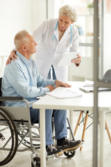 Fototapeta premium Portrait of female doctor consulting handicapped elderly man, copy space