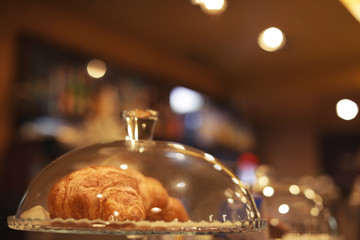 Glass cloche and plate with croissants on counter in cafe. Space for text