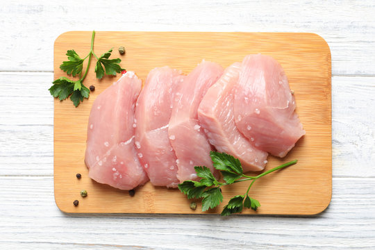 Board with cut raw turkey fillet and parsley on white wooden background, top view