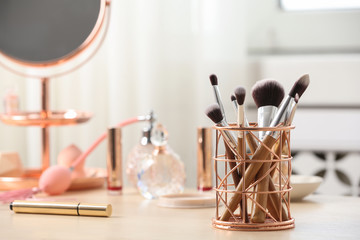 Holder with different makeup brushes on dressing table, space for text