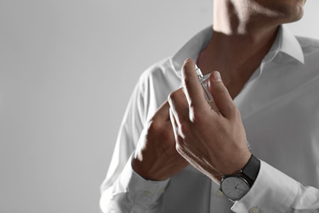 Handsome man applying perfume on neck against light background, closeup. Space for text