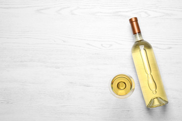 Glass and bottle with white wine on wooden background, flat lay. Space for text