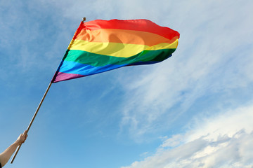 Gay man holding rainbow LGBT flag against blue sky. Space for text