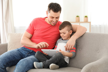 Boy and his father with tablet sitting on sofa at home. Family time