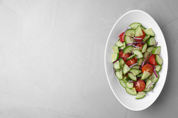 Plate of vegetarian salad with cucumber, tomato and onion on light background, top view. Space for text