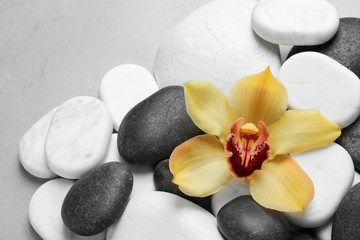 Beautiful orchid flower among different spa stones on table, top view. Space for text