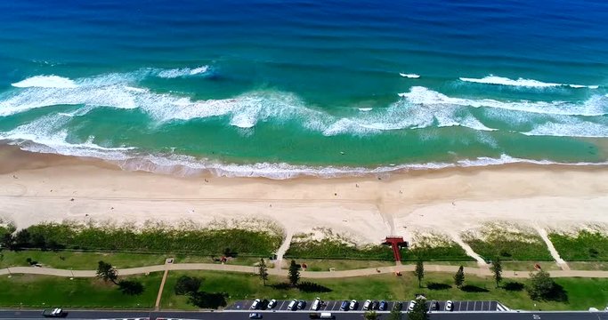 Forward, top view, drone shot of ocean waves crashing on the sandy shore near Miami suburb, Queensland, Australia, on a sunny day