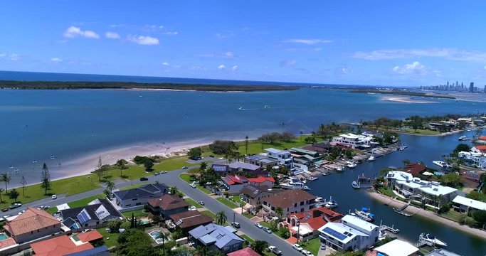 Drone shot of Runaway Bay, Queensland, Australia, with the beach between a bright and clean ocean, and buildings, on a sunny day with some clouds