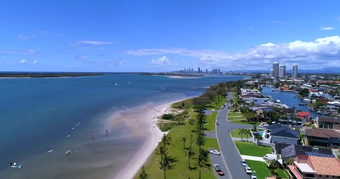 Drone shot of Runaway Bay, Queensland, Australia, with surfers waiting for waves in the bright and clean ocean, with the city in the background, on a sunny day with some clouds