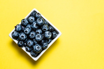 Fresh blueberries inside pot on yellow background.