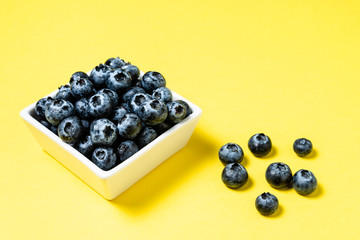 Fresh blueberries inside pot on yellow background.