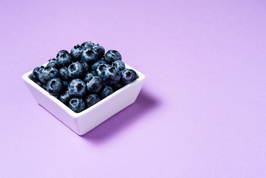 Fresh blueberries inside pot on purple background.