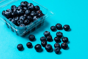 Fresh blueberries inside plastic container on blue background.