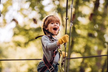 Little child climbing in adventure activity park with helmet and safety equipment. Toddler climbing in a rope playground structure