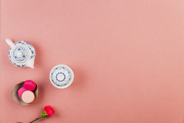Pink and fuchsia french macarons in a bowl with fuchsia incarnation flower and chinaware teapot and bowl over a pink tablecloth background with copyspace.