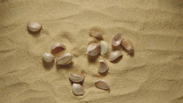 SLOW MOTION: Garlic cloves fall onto a heap of garlic powder