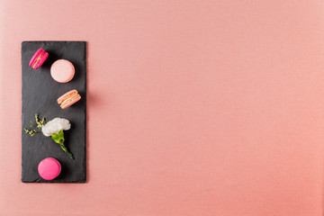 French pink macarons or macaroons, and incarnation white flower on a slate over a pink tablecloth background with copyspace. - Powered by Adobe