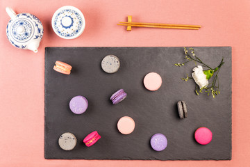 French macarons or macaroons, and incarnation white flower on a slate, with chopsticks and traditional chinaware teapot and tea bowl.