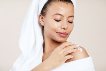 Head and shoulders portrait of  elegant Mixed-Race woman applying body cream during morning routine, copy space