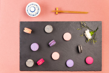 French macarons or macaroons, and incarnation white flower on a slate, with chopsticks and traditional chinaware tea bowl.