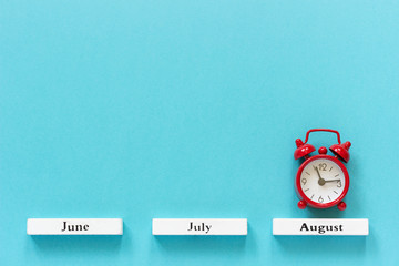 Wooden calendar summer months and red alarm clock over August on blue background. Concept August...
