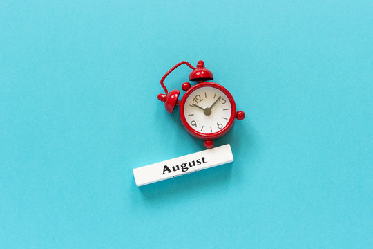 Wooden calendar summer month August and red alarm clock on blue paper background. Concept Hello August or Good bye August Creative Top view Flat Lay Minimal style.